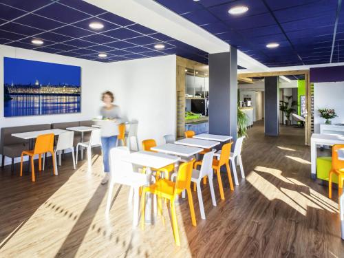 una mujer parada en un restaurante con mesas y sillas en ibis budget Bordeaux Est Lormont, en Lormont