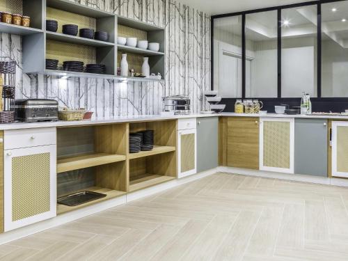 a kitchen with white cabinets and wooden shelves at Mercure Orléans Portes de Sologne in Ardon