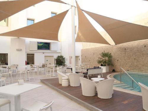 a patio with white tables and chairs and a pool at Ibis Sfax in Sfax