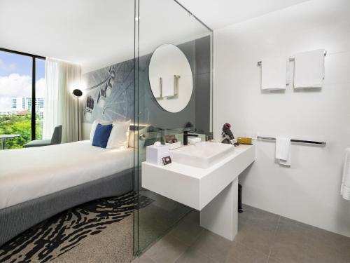 Un baño con una cama, un lavabo y un espejo. en Novotel Brisbane South Bank, en Brisbane