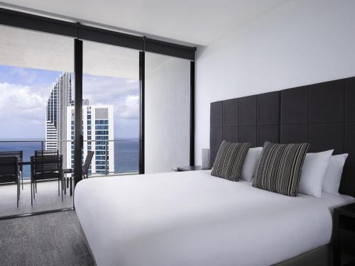 a bedroom with a large white bed and a balcony at Mantra Circle On Cavill in Gold Coast