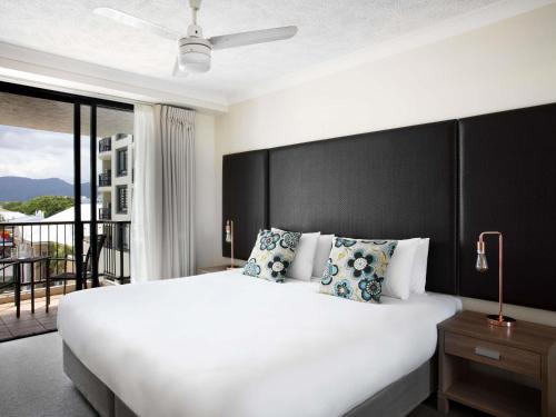 a bedroom with a large white bed and a balcony at Mantra Esplanade in Cairns