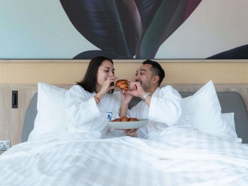 un hombre y una mujer sentados en la cama comiendo comida en Novotel Sihanoukville Holiday Resort, en Sihanoukville