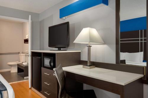 Cette chambre comprend un bureau avec une télévision et une lampe. dans l'établissement Baymont by Wyndham Albany at Albany Mall, à Albany