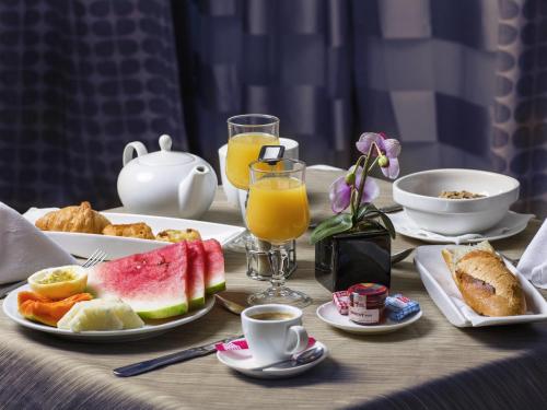 Una mesa cubierta con platos de desayuno y jugo de naranja. en Mercure Cayenne Royal Amazonia, en Cayenne