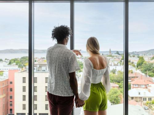 a man and a woman looking out of a large window at Ibis Styles Hobart in Hobart