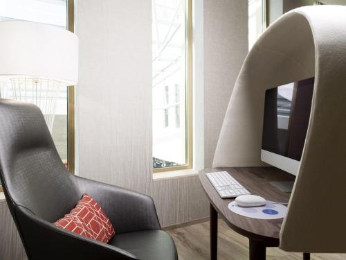 Una habitación con una silla y una computadora en un escritorio. en Novotel Charleroi Centre, en Charleroi