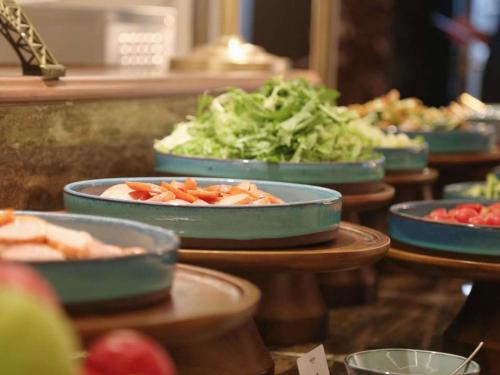 北京北京安贞奥体中心美居酒店的自助餐台上摆放着盛在蓝色碗里的蔬菜食物。