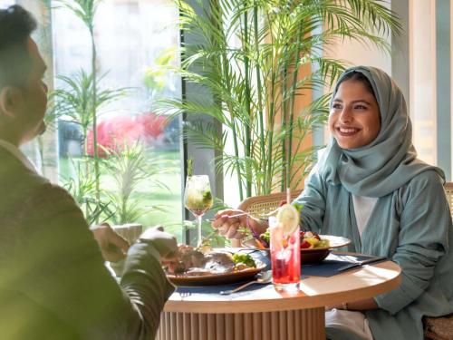 una mujer sentada en una mesa comiendo comida en Swissotel Living Jeddah, en Yeda