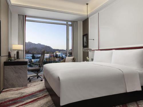 a bedroom with a large white bed and a large window at Movenpick by Accor Qingdao Sunmei in Qingdao