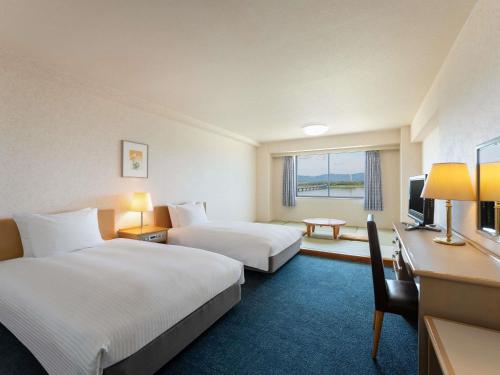 a hotel room with two beds and a desk at Grand Mercure Lake Hamana Resort & Spa in Hamamatsu
