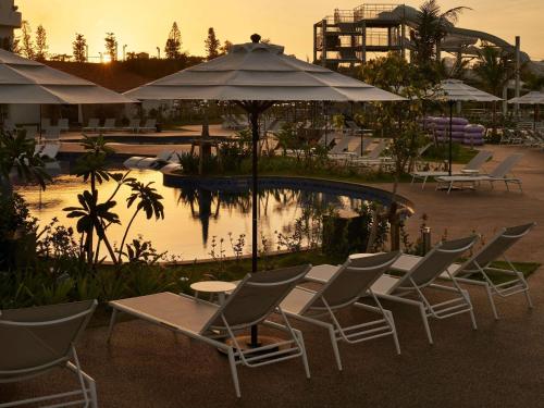 a group of chairs and tables with umbrellas next to a pool at Grand Mercure Okinawa Cape Zanpa Resort in Yomitan