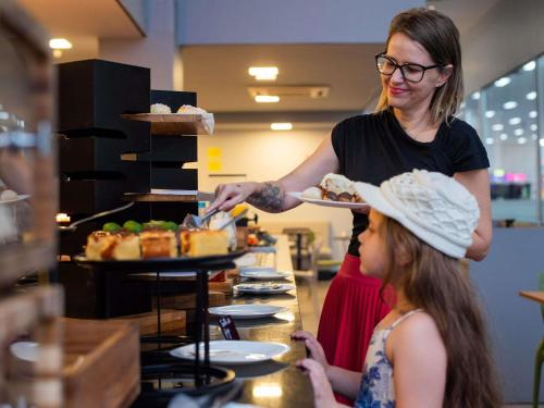 Una mujer dándole un plato de comida a un niño. en ibis Styles Goiânia Shopping Estação, en Goiânia