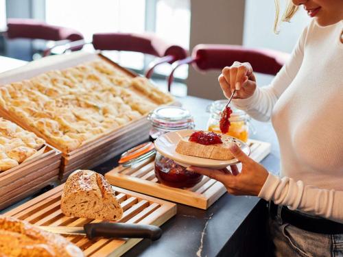 Eine Frau isst ein Stück Brot mit Marmelade. in der Unterkunft TRIBE Manchester Airport by Accor in Hale
