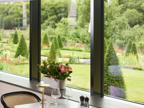 una mesa con dos sillas y un jarrón con flores en una ventana en Domaine du Liziec Vannes - MGallery Collection, en Vannes