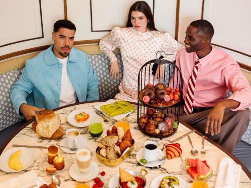 Un grupo de tres personas sentadas alrededor de una mesa con comida. en SLS Barcelona, en Barcelona