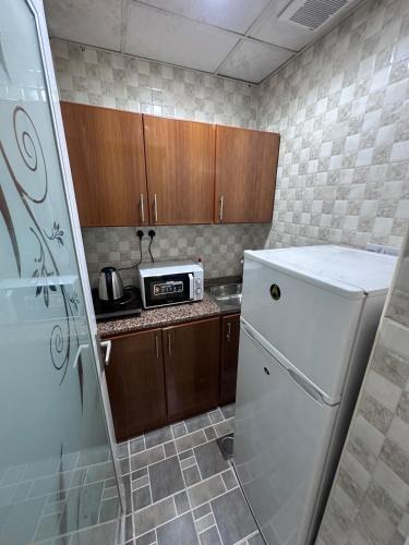 a small kitchen with a white refrigerator and wooden cabinets at Studio room in Al ain in Al Ain