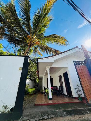 a white house with a palm tree in front of it at Uvindu Villa - Cozy By Midigama in Weligama