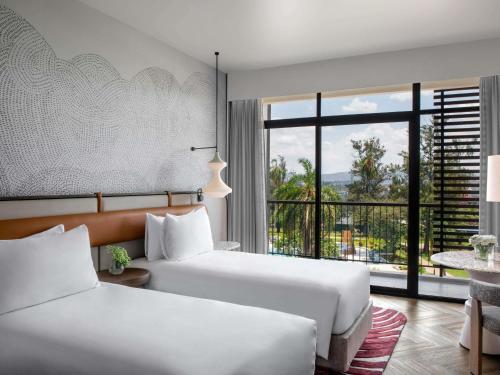 two beds in a hotel room with a large window at Mövenpick Kigali in Kigali
