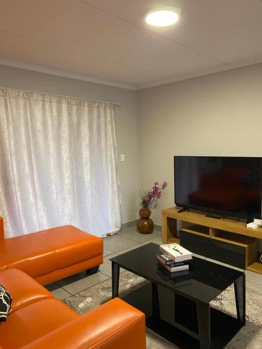 ein Wohnzimmer mit einem orangenen Sofa und einem Flachbild-TV in der Unterkunft Unmatched Stays in Kempton Park