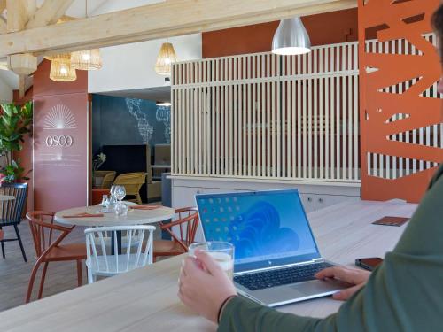 una persona sentada en una mesa con un ordenador portátil en ibis Styles Aubagne Gemenos, en Gémenos