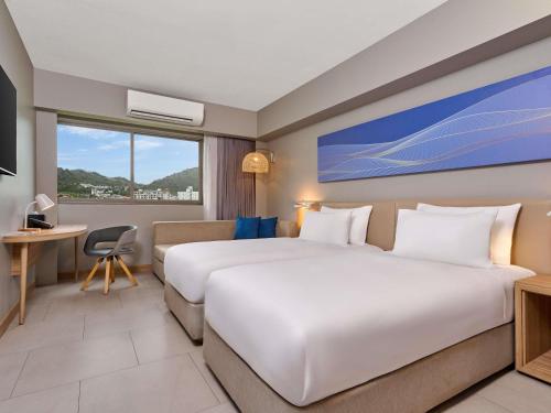 a hotel room with two beds and a desk at Mercure Phuket Patong Journeyhub in Patong Beach