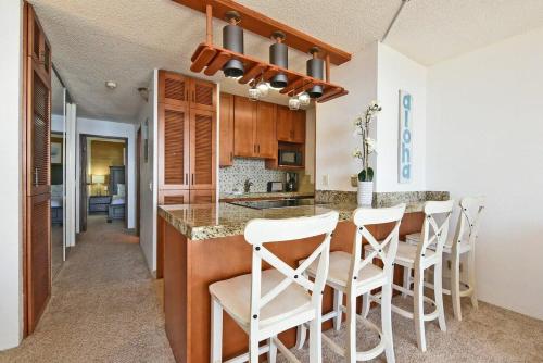 a kitchen with a bar with white chairs in it at Maalaea Banyans 203 · MBN 203 OceanFront 1BD Amazing Ocean Views in Wailuku