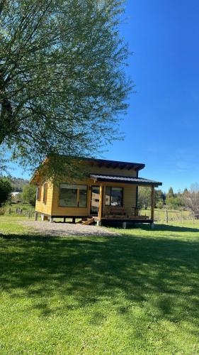 a small house in a field with a tree at Cabaña Lilacho in Cholila