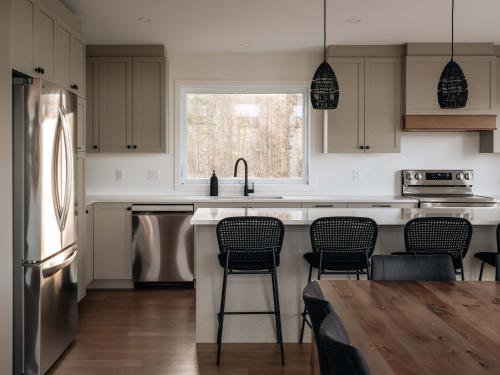 a kitchen with a sink and a counter with chairs at Chalet a Samia - Spa, luxury, Jay Peak view in Mansonville
