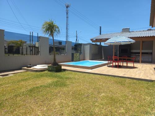 a backyard with a pool and a table and an umbrella at Casa Com Quatro Dormitórios, Pertinho Do Mar Em Capão Da Canoa in Capão da Canoa
