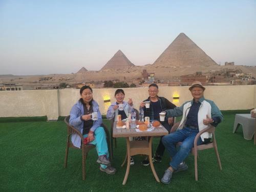 een groep mensen die aan een tafel voor piramiden zitten bij The Tree Pyramids Inn in Caïro