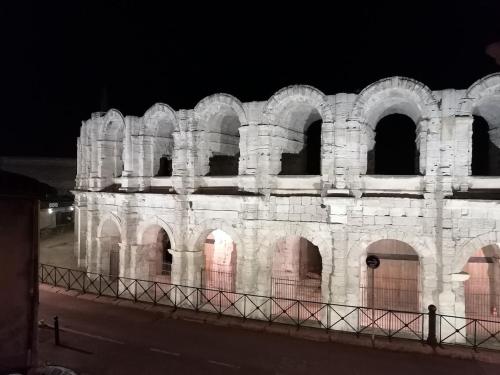 阿尔勒Extraordinaire face aux Arènes的夜晚，一座带有拱形入口的大型石砌建筑映入眼帘。