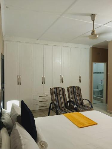a bedroom with two chairs and a bed and cabinets at Mhlezi Lodge in Richards Bay
