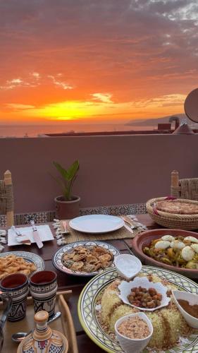 Una mesa con platos de comida con la puesta de sol. en taghoba surf house, en Tamraght Ouzdar