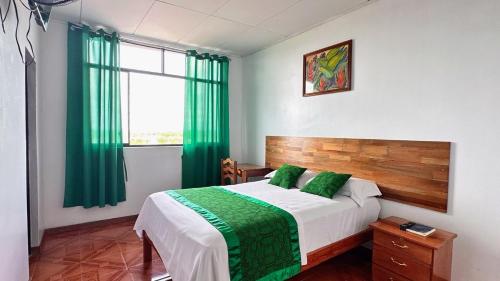 a bedroom with a bed with green curtains and a window at Hostal Maravilla Amazónica in Iquitos
