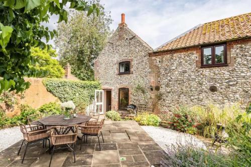 un patio avec une table et des chaises devant un bâtiment dans l'établissement Mulberry Coach House, à East Rudham