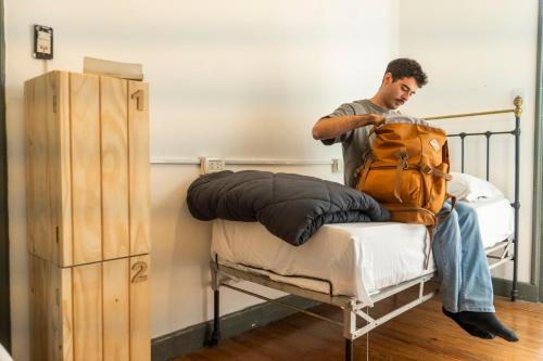un uomo seduto su un letto con uno zaino di Hostel Punto Andino Salta a Salta