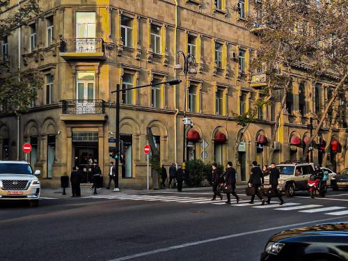 バクーにあるAlara Hotel INNの建物前の道を横断する人々