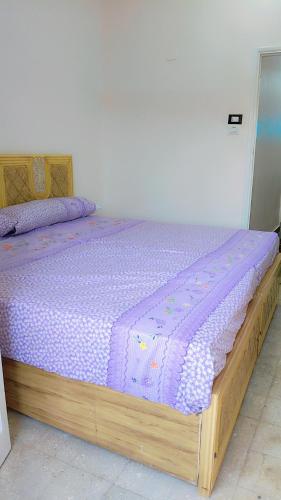 un lit en bois avec une couette violette dessus dans l'établissement Atlas Aswan Apartment Near Nile Corniche and Old Tourist Market شقة أطلس أسوان بجوار كورنيش النيل والسوق السياحي القديم, à Assouan