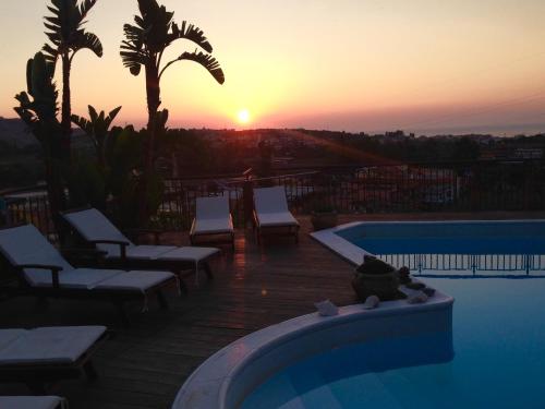 a sunset over a swimming pool with chairs and a cat sitting on the edge at Villa Carly Taormina apartment with private pool in Trappitello