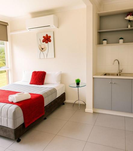 a bedroom with a bed with a red blanket and a sink at Motel Traralgon in Traralgon
