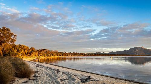 einen Strand mit einem Wasserkörper mit Bäumen und Bergen in der Unterkunft Bluff House Flinders Island Tasmania in Whitemark