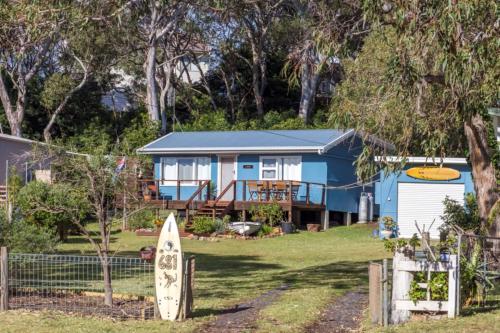 a blue house with a surfboard in front of it at Retro Beach Cottage - classic surf getaway in Kioloa