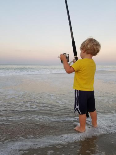 a young boy standing on the beach holding a fishing rod at First Colony Inn in Nags Head