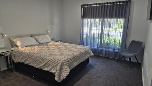 a bedroom with a bed and a chair and a window at Silverwood 17th Hole Retreat in Yarrawonga