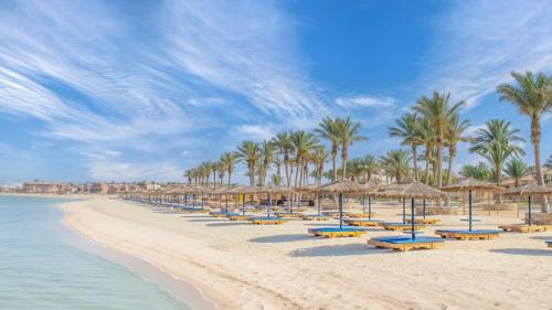 ein Strand mit Stühlen, Sonnenschirmen und Palmen in der Unterkunft Protels Crystal Beach Resort in Marsa Alam City