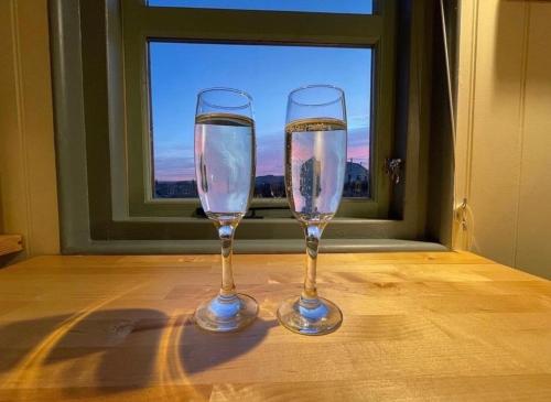 two wine glasses sitting on a table in front of a window at Cornwall Shepherds Hut - Hot Tub & Cosy Log Burner in Saint Day