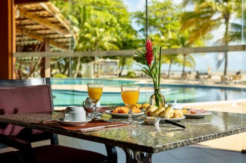 a table with food and drinks and a pool at Hotel Karapitangui in Morro de São Paulo