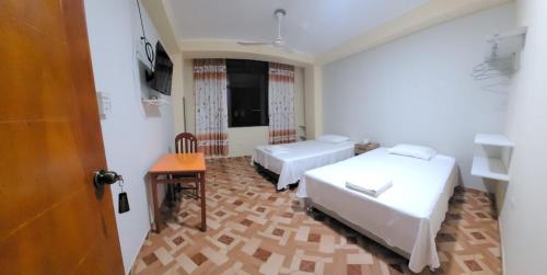 une chambre avec deux lits, une table et une porte dans l'établissement Hospedaje Luciana, à Pucallpa