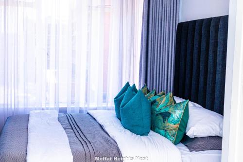 a bed with blue and white pillows in front of a window at MoffatHeights Nest in Harare